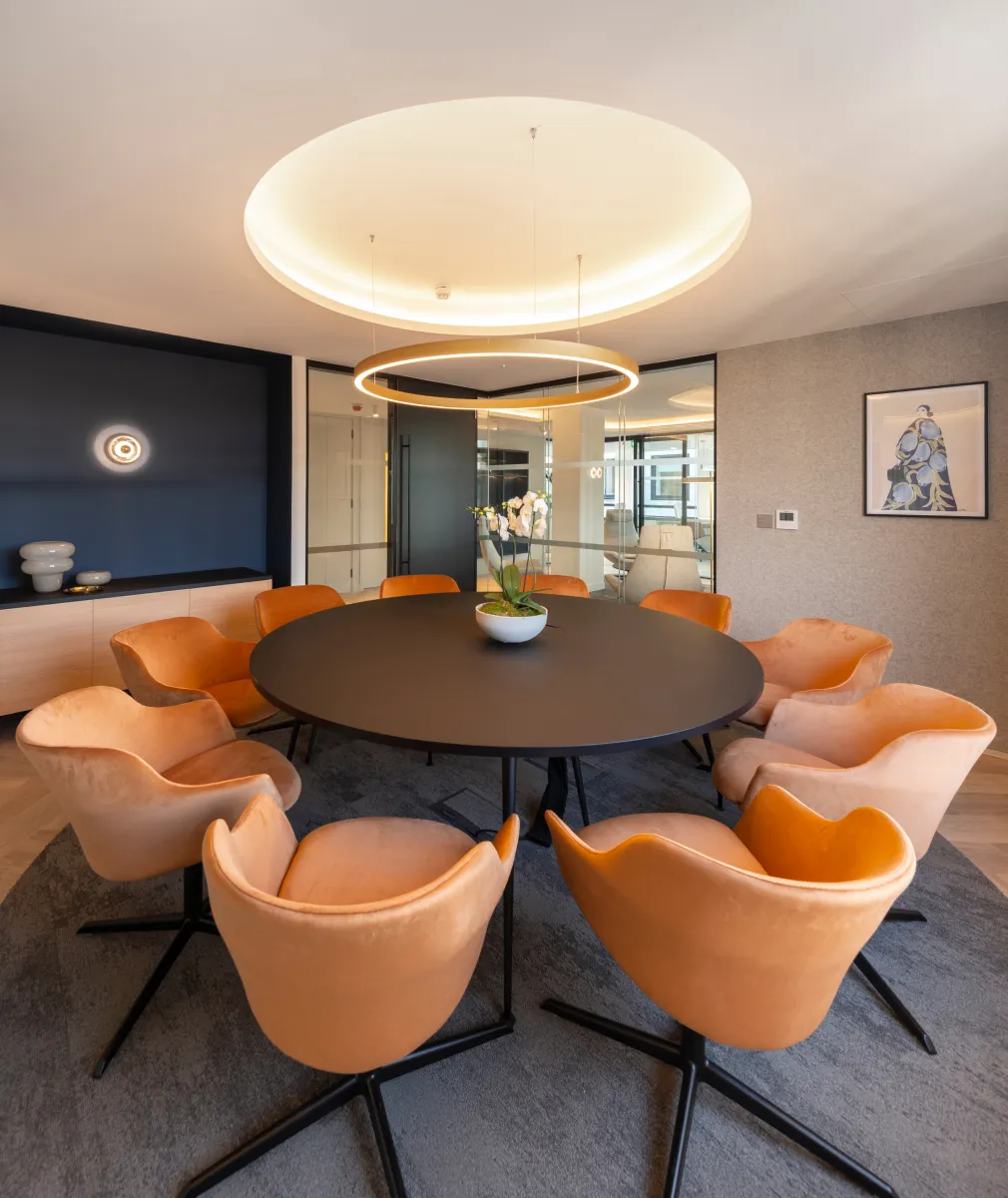 Commercial office refurbishment with round table and orange chairs around it.