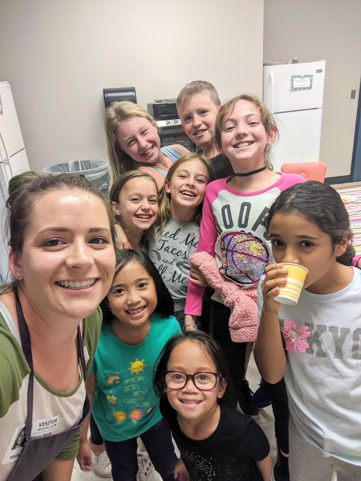 A woman takes a smiling selfie with a group of eighth cooking class students.