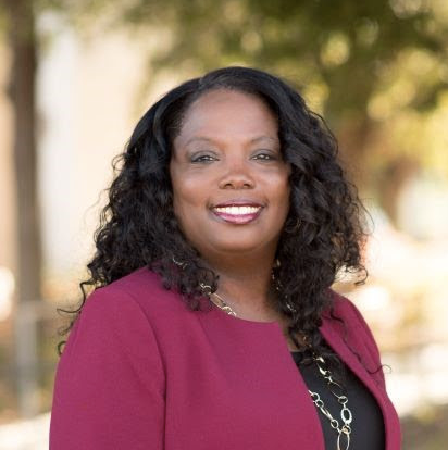 An African-American woman wearing a pink blazer smiles at the camera. 