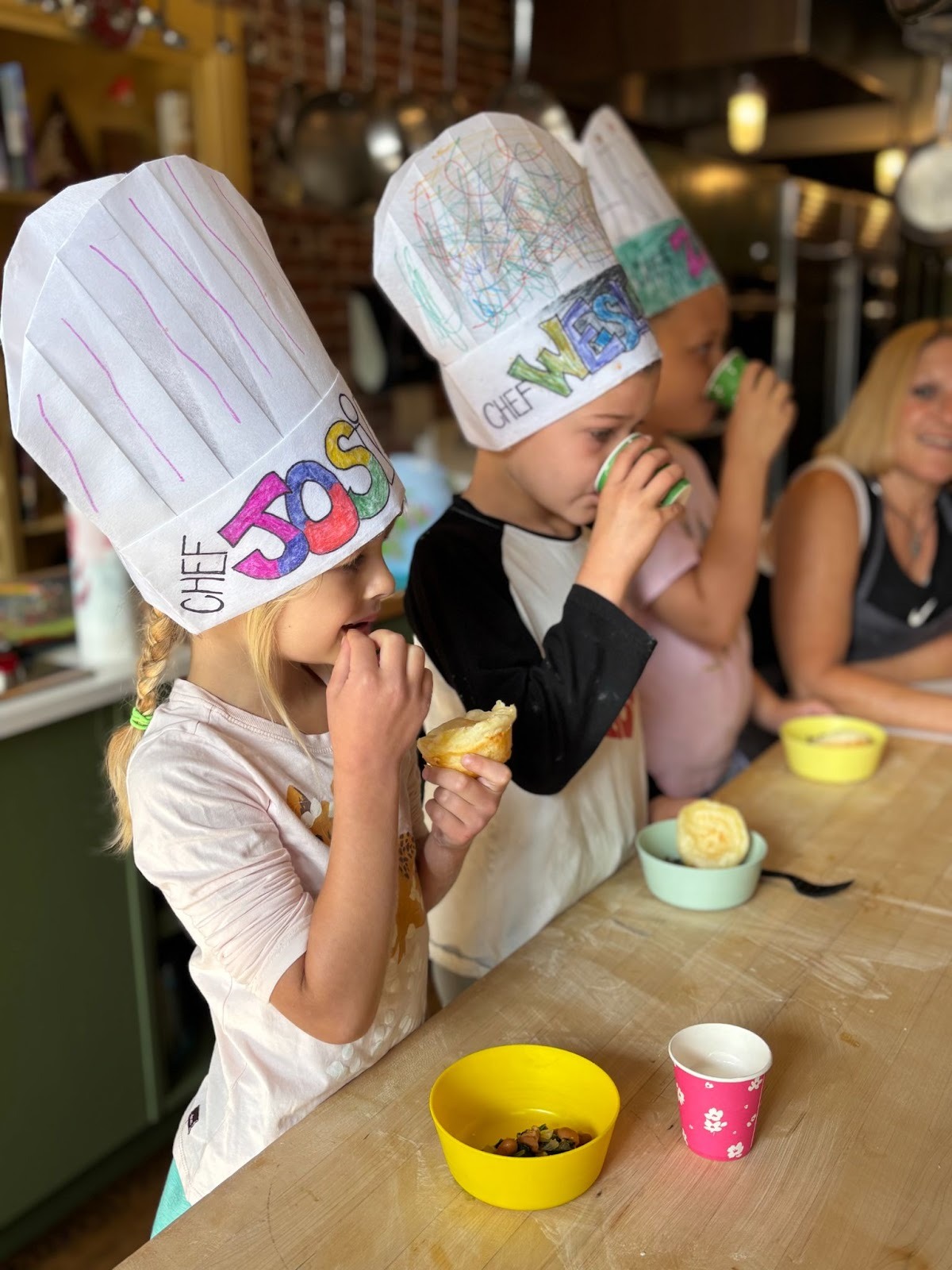 Three young children taste food and drinks during a Sticky Fingers Cooking summer camp.