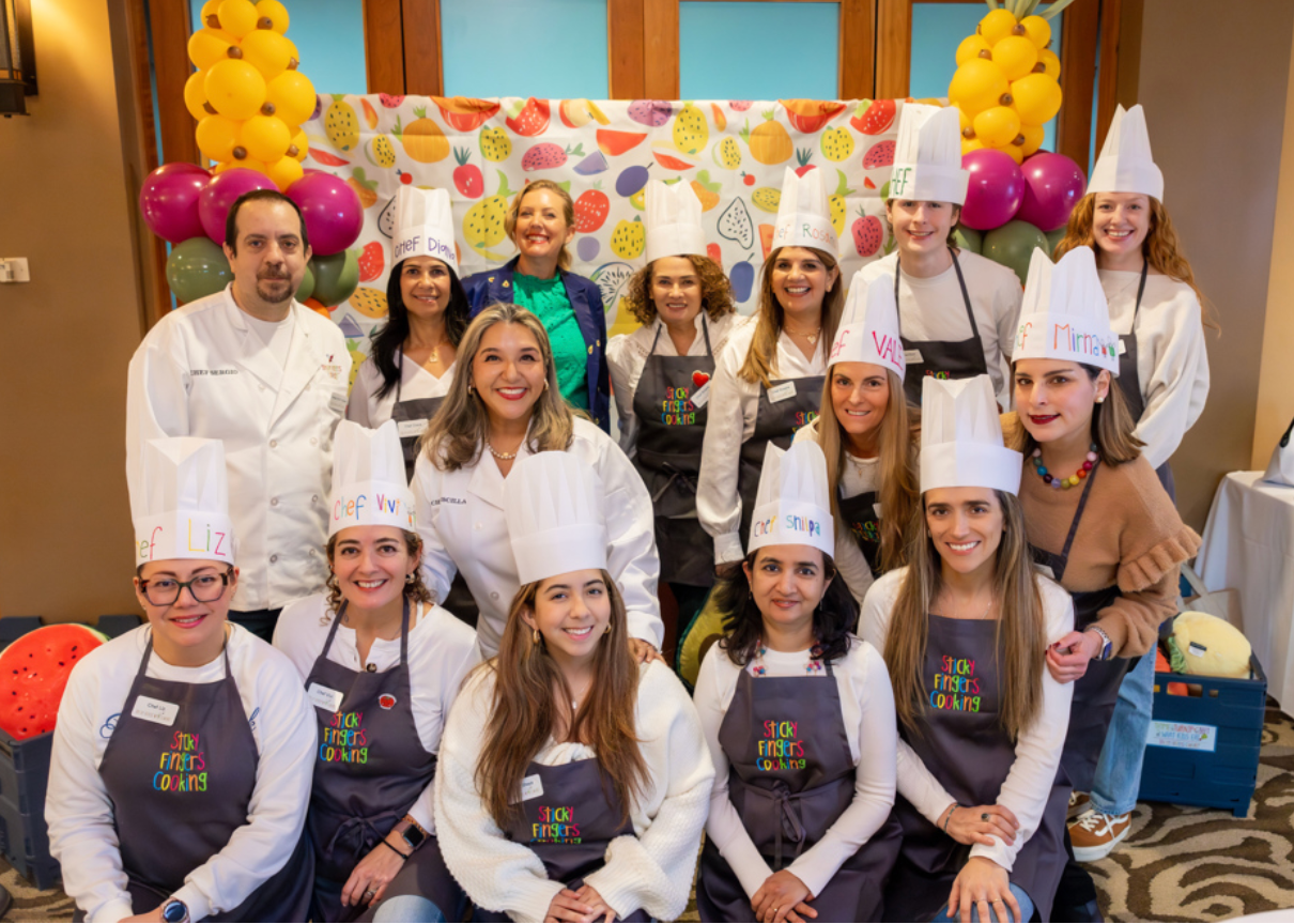 A group of several people in white chef hats and kitchen aprons smile at the camera during the grand opening of Sticky Fingers Cooking of Seattle East. 