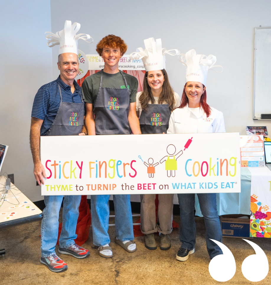 Two smiling men and two smiling women hold a sign that reads, “Sticky Fingers Cooking” in front of them. 
