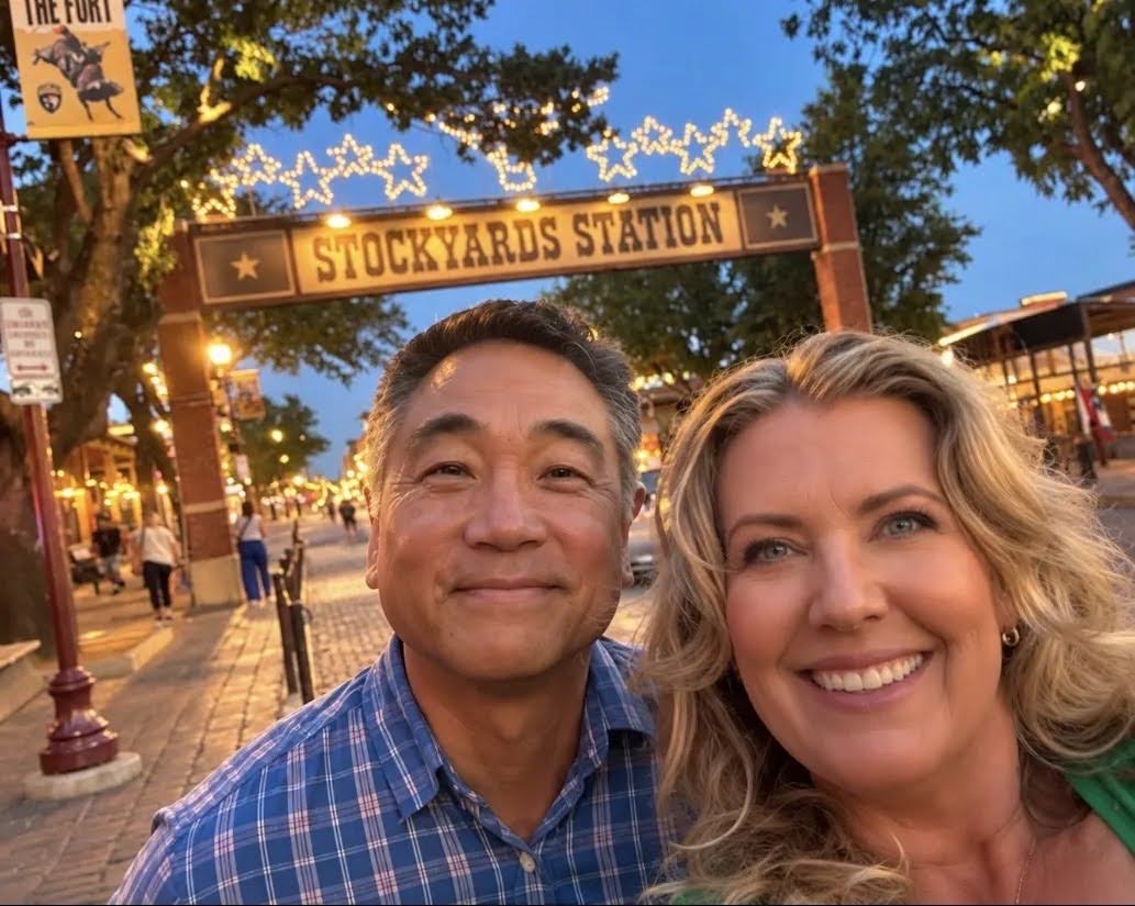 Man and woman take a selfie while smiling at the camera, there's a large street with a Stockyard Station sign in the background