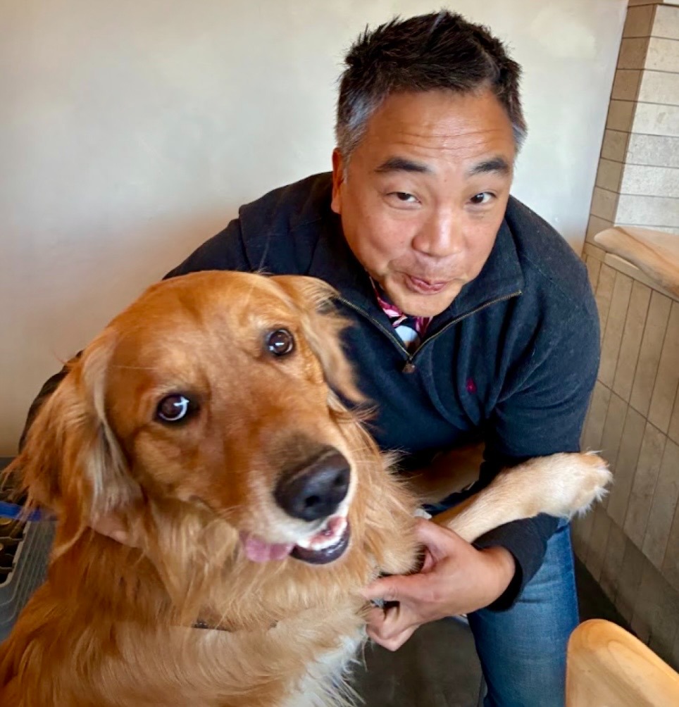 A man in a black pullover smiles for a photo with a dog that also appears to be smiling for the camera.