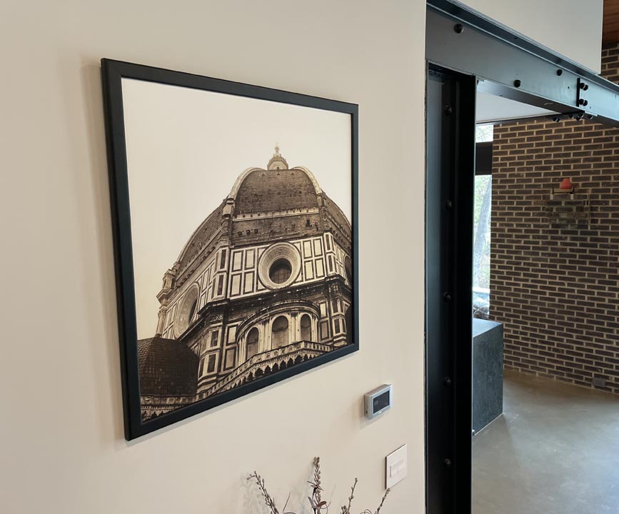 Framed sepia-toned photograph of a historic domed building with ornate architectural details hanging on a beige wall next to a modern black metal sliding door track.