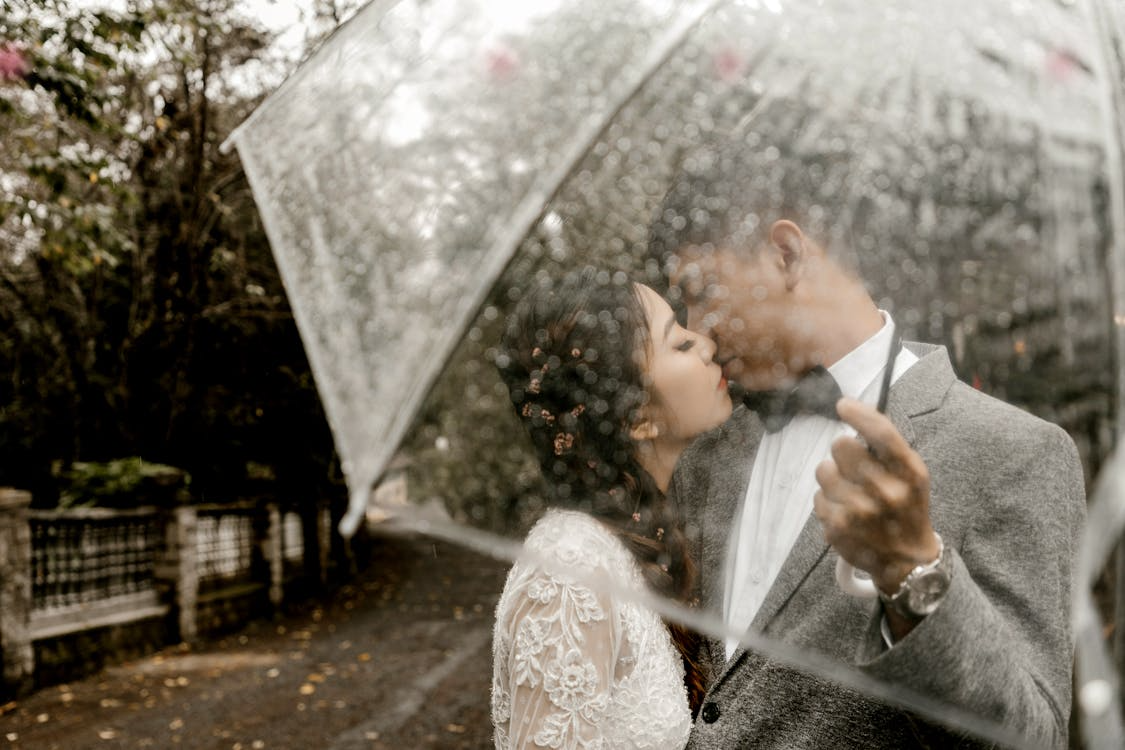 Bride and groom kissing under a clear umbrella during a rainy spring wedding