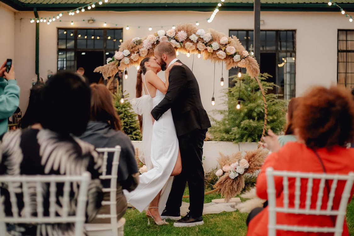 Bride and groom kissing under a floral arch at an outdoor spring wedding ceremony