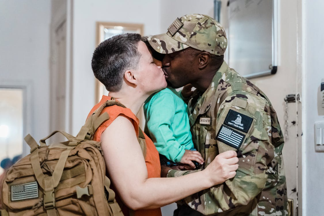 Military spouse benefits during deployment, service member kissing family goodbye before leaving for duty.