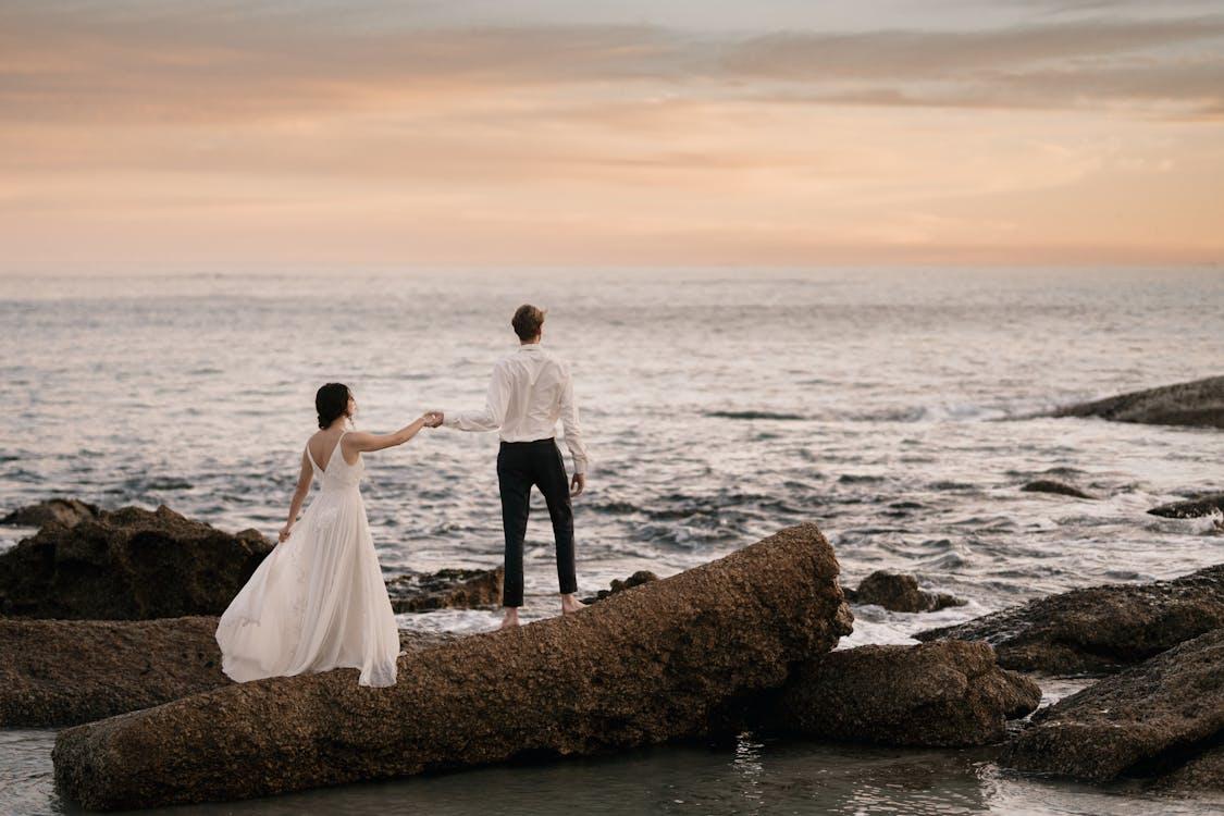Benefits of getting married, couple standing on coastal rocks at sunset after their wedding ceremony.