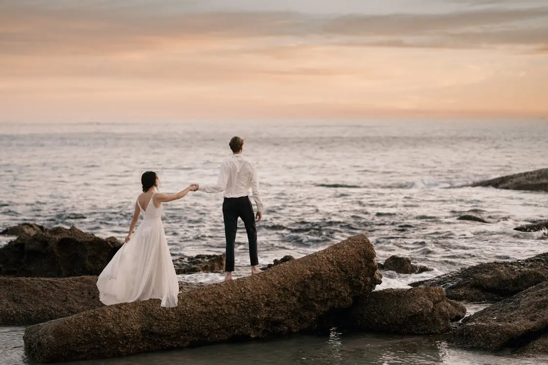 Benefits of getting married, couple standing on coastal rocks at sunset after their wedding ceremony 