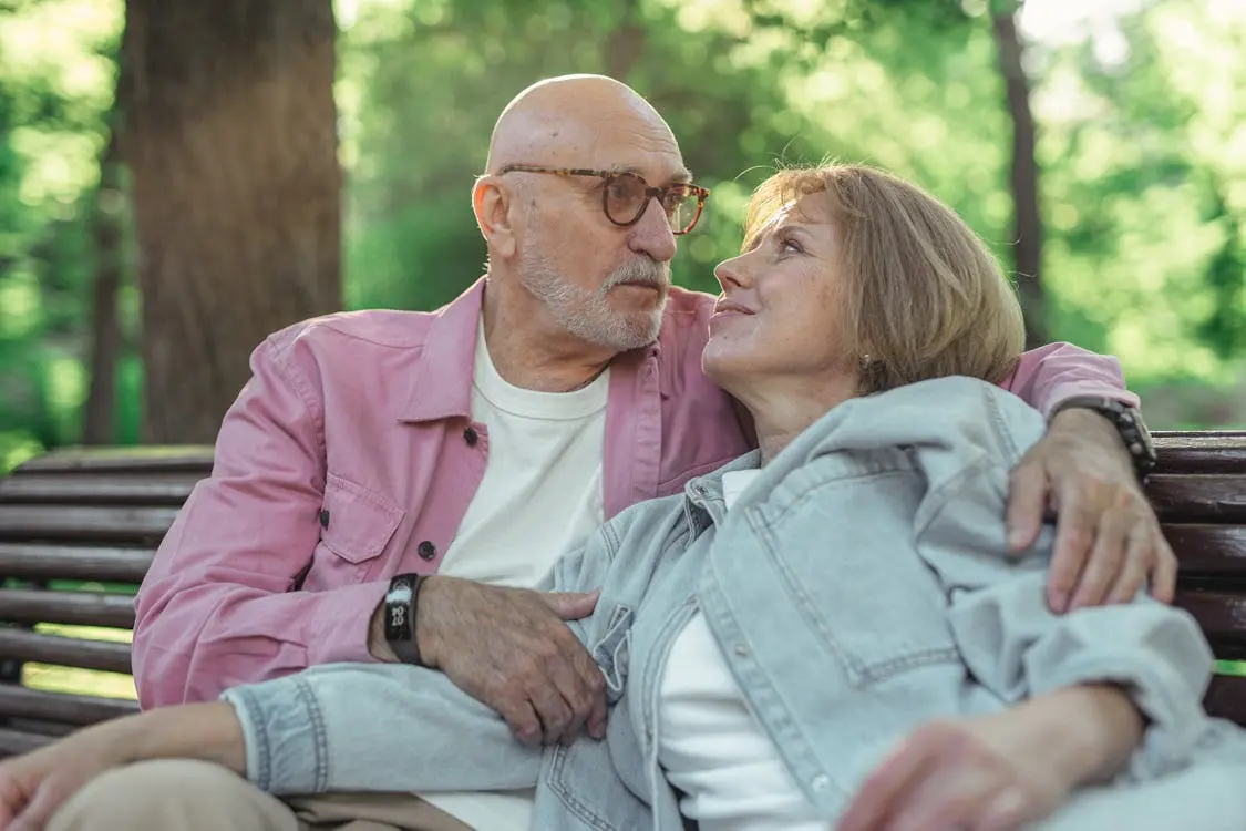 Health benefits of getting married illustrated by an older married couple sharing emotional support on a park bench .
