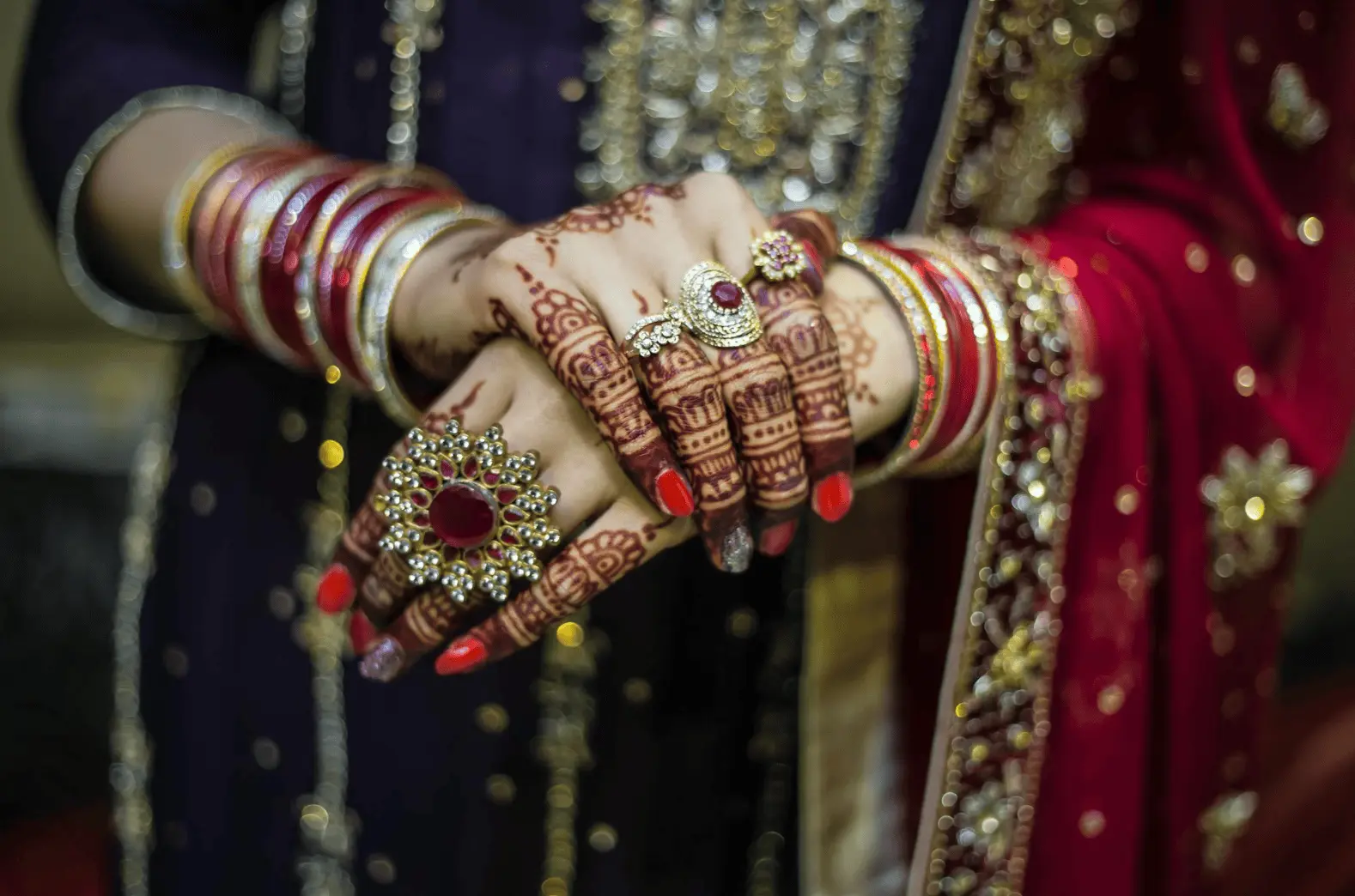 Woman wearing a red and gold dress holding up henna decorated hands: wedding night traditions.