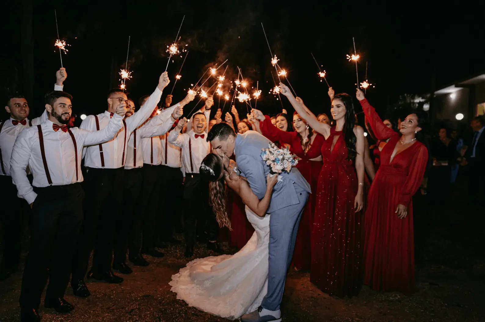 Modern wedding with groom kissing bride with friends holding up sparklers: wedding night traditions.
