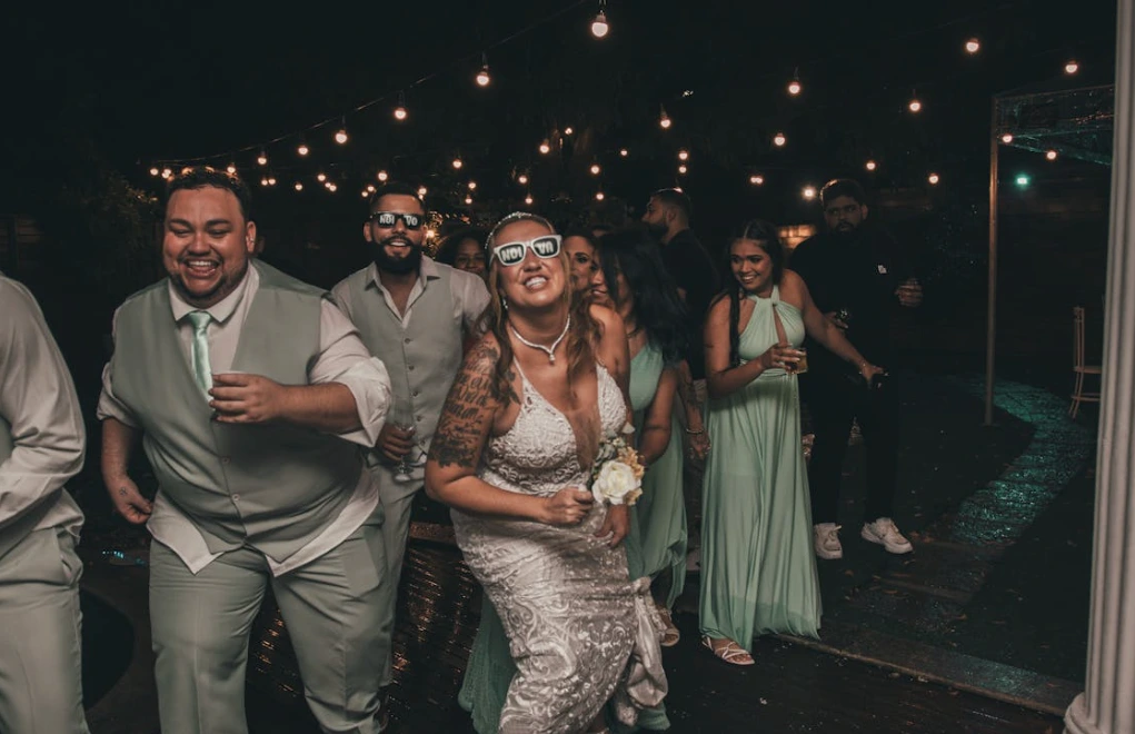 Bride and groom dancing with guests at wedding party while wearing sunglasses.