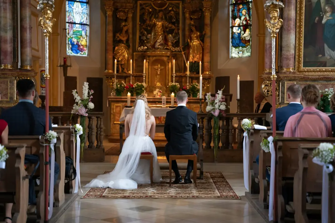 Bride and groom seated at the front of the church aisle waiting to be married: Catholic wedding traditions.
