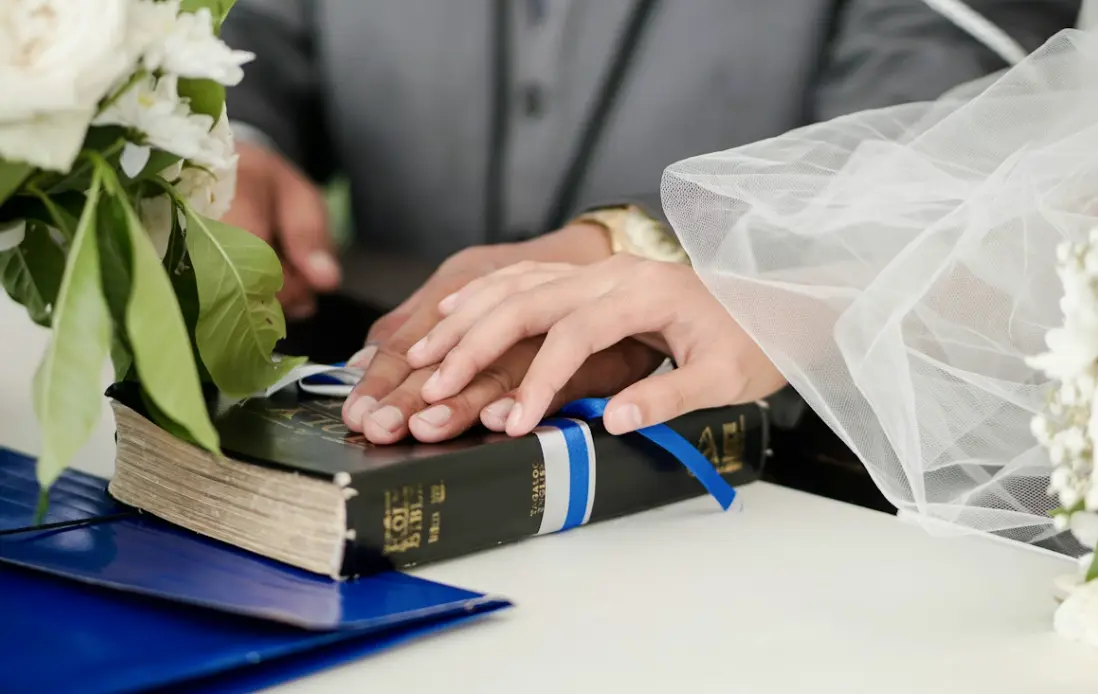 Man and woman’s hands on top of the Holy Bible during a wedding ceremony: Catholic wedding traditions.