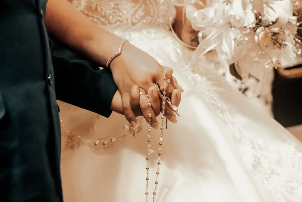 Bride and groom at wedding holding hands with rosary entwined between them: Catholic wedding traditions.