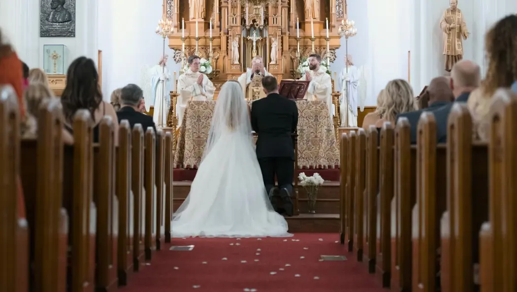 Bride in wedding dress and groom in suit kneeling at the altar of a Catholic church: Catholic wedding traditions.