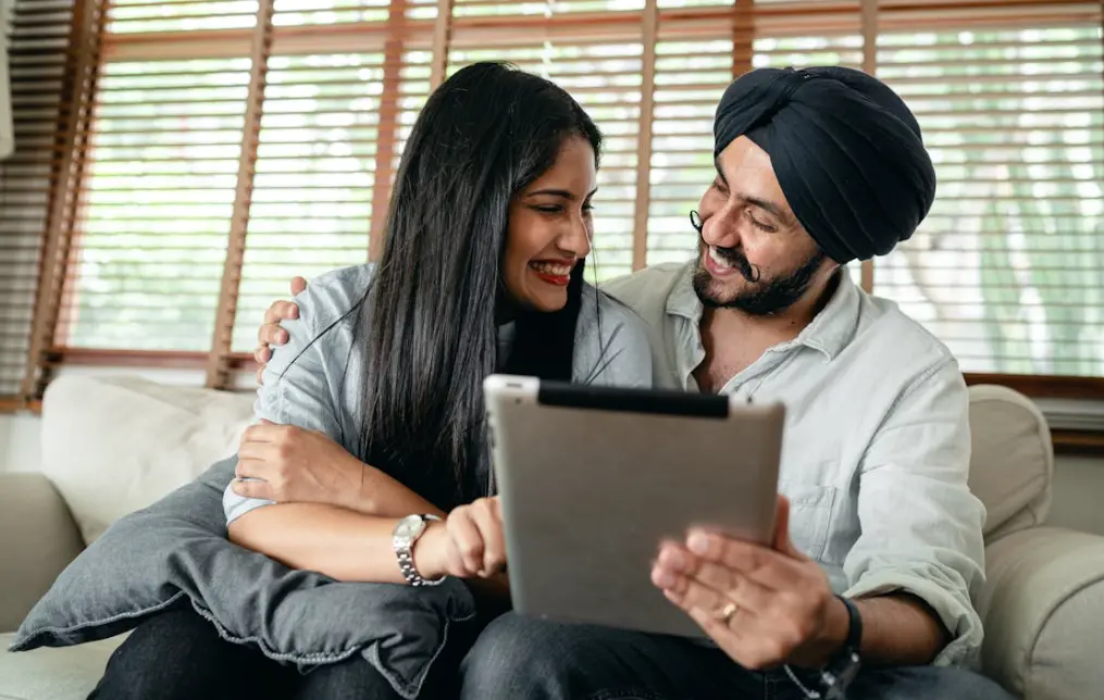  Couple sitting on couch and smiling while interacting with a tablet: can I get married online?