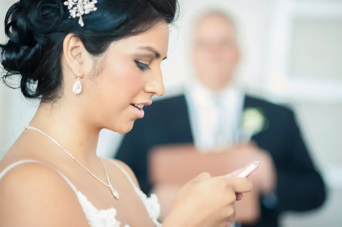 Bride in foreground using her phone with the groom in the background: can I get married online using Zoom? 