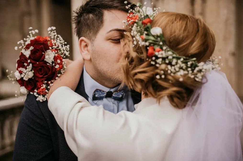 Newlyweds kissing after being married; bride holding a bouquet of flowers: getting married online. 