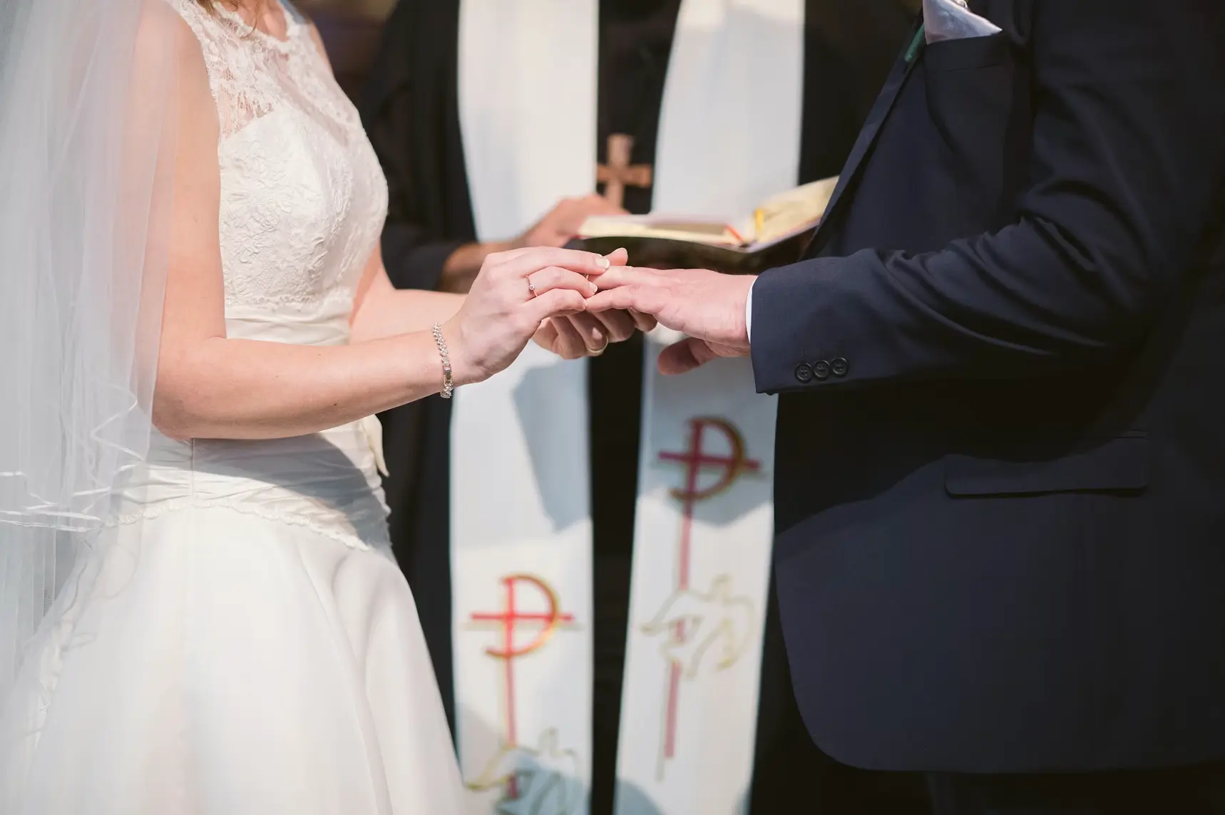 Catholic bride and groom holding hands and placing rings on fingers during biblical marriage.