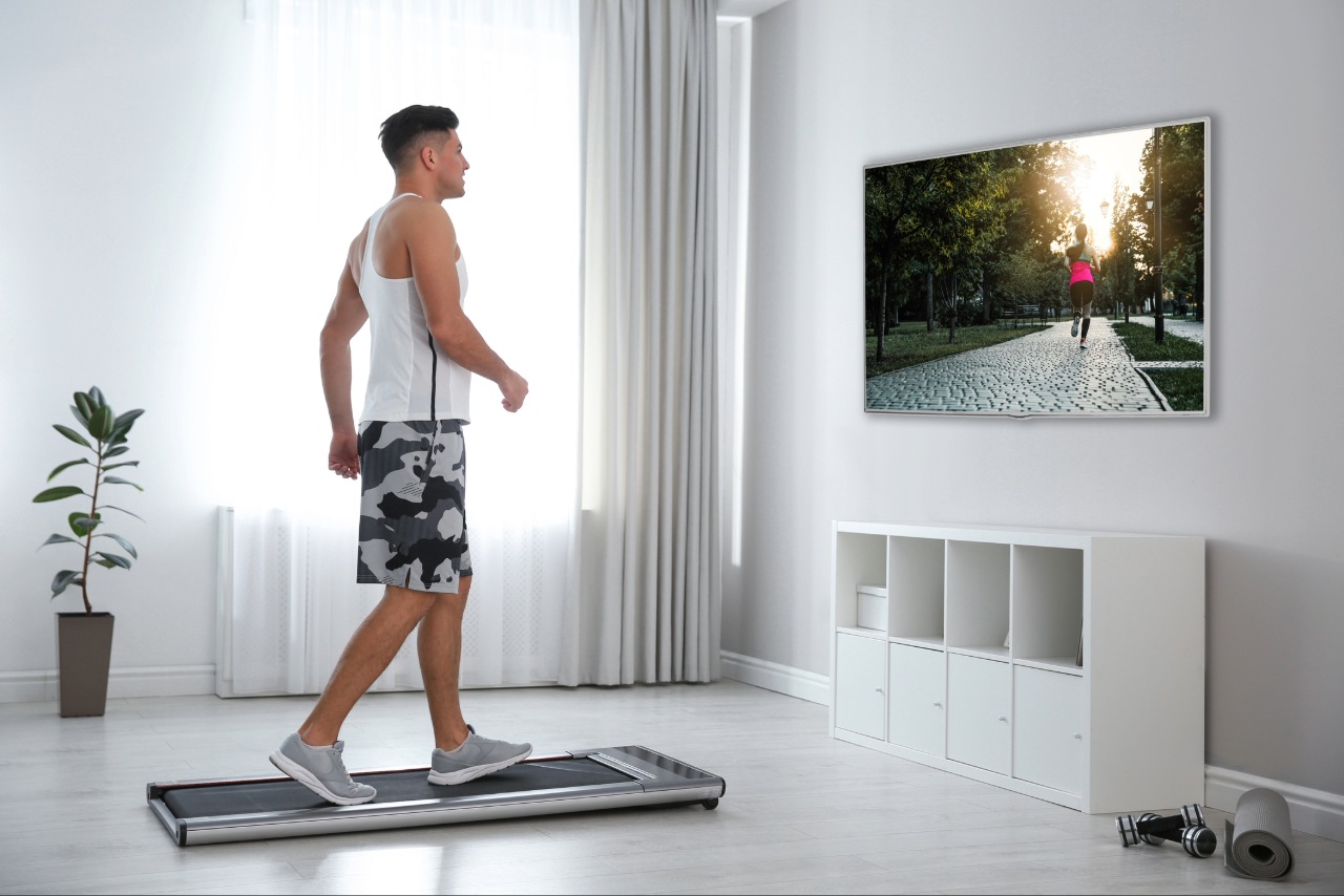 A man walking on a walking pad in his home whilst watching TV.