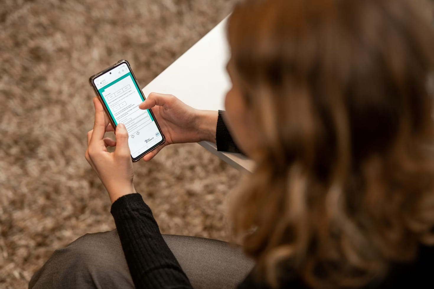 Person holding a smartphone with a survey or form on the screen while sitting on a carpet.