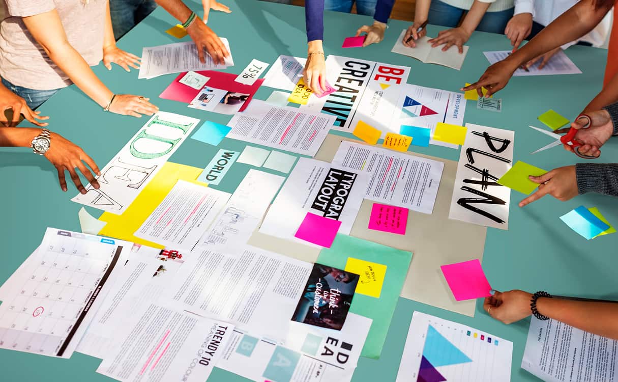 People collaborating around a table covered with documents, charts, and colorful sticky notes.