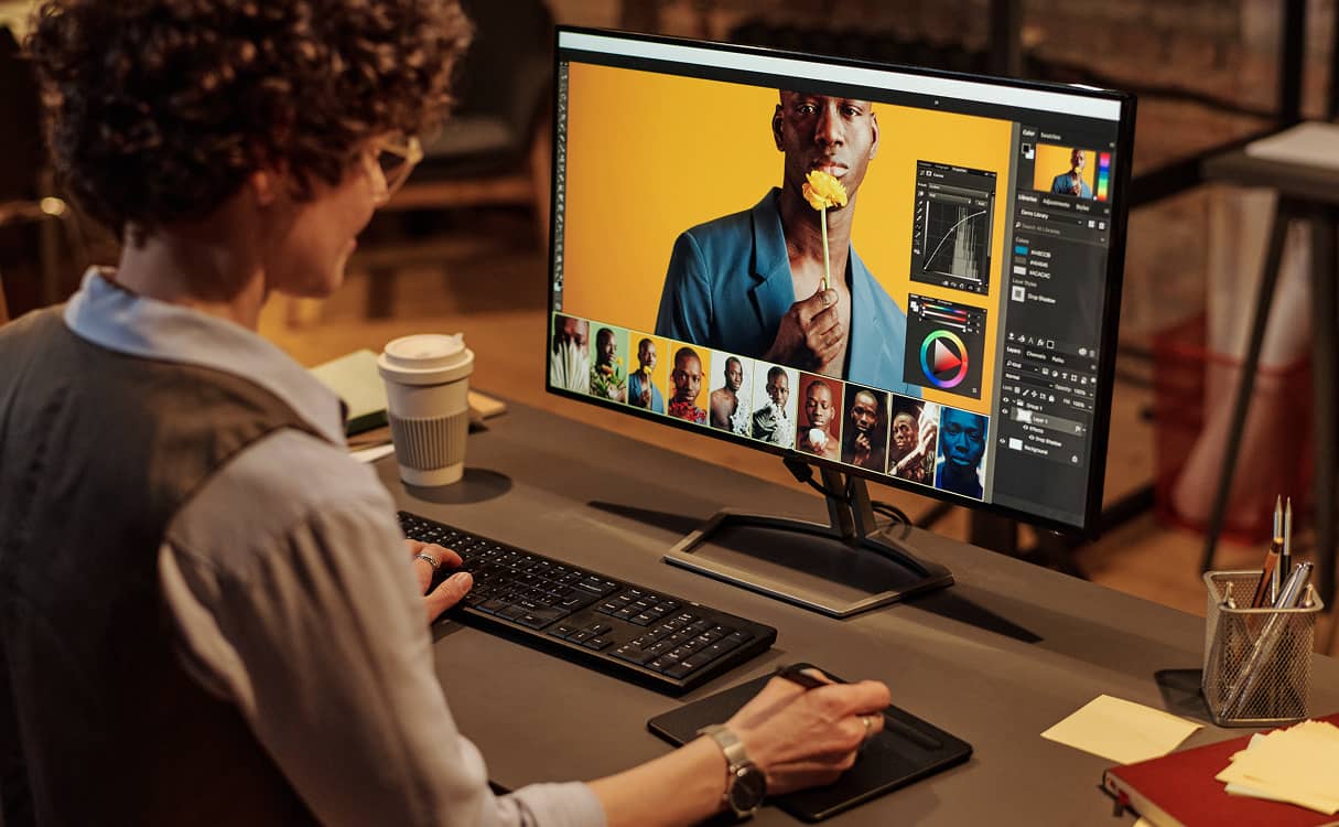 Person editing a portrait photo of a man holding a yellow flower on a desktop monitor using a drawing tablet.