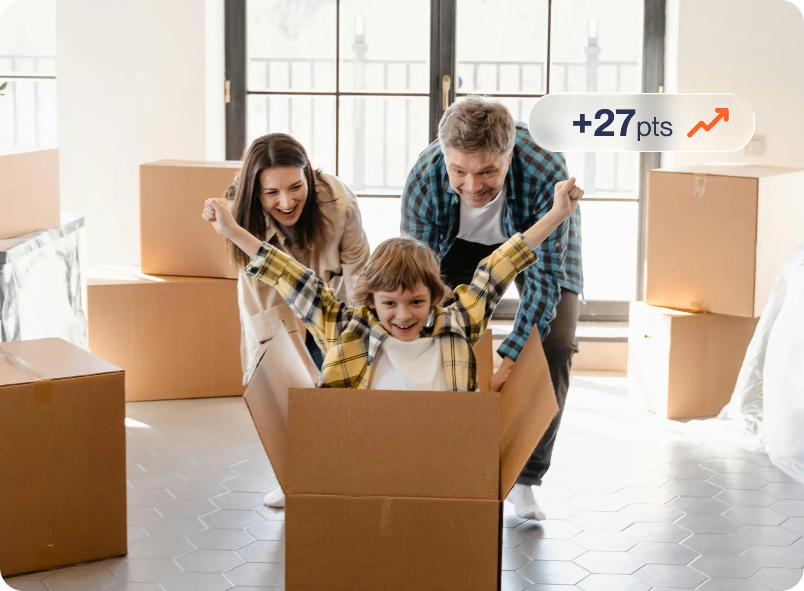 Child with arms raised joyfully sitting inside a cardboard box, pushed by two smiling adults amid packed moving boxes with a credit score graphic.