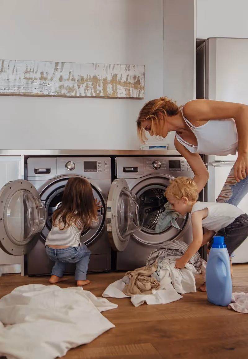 woman loading a washing machine and dryer with two kids.