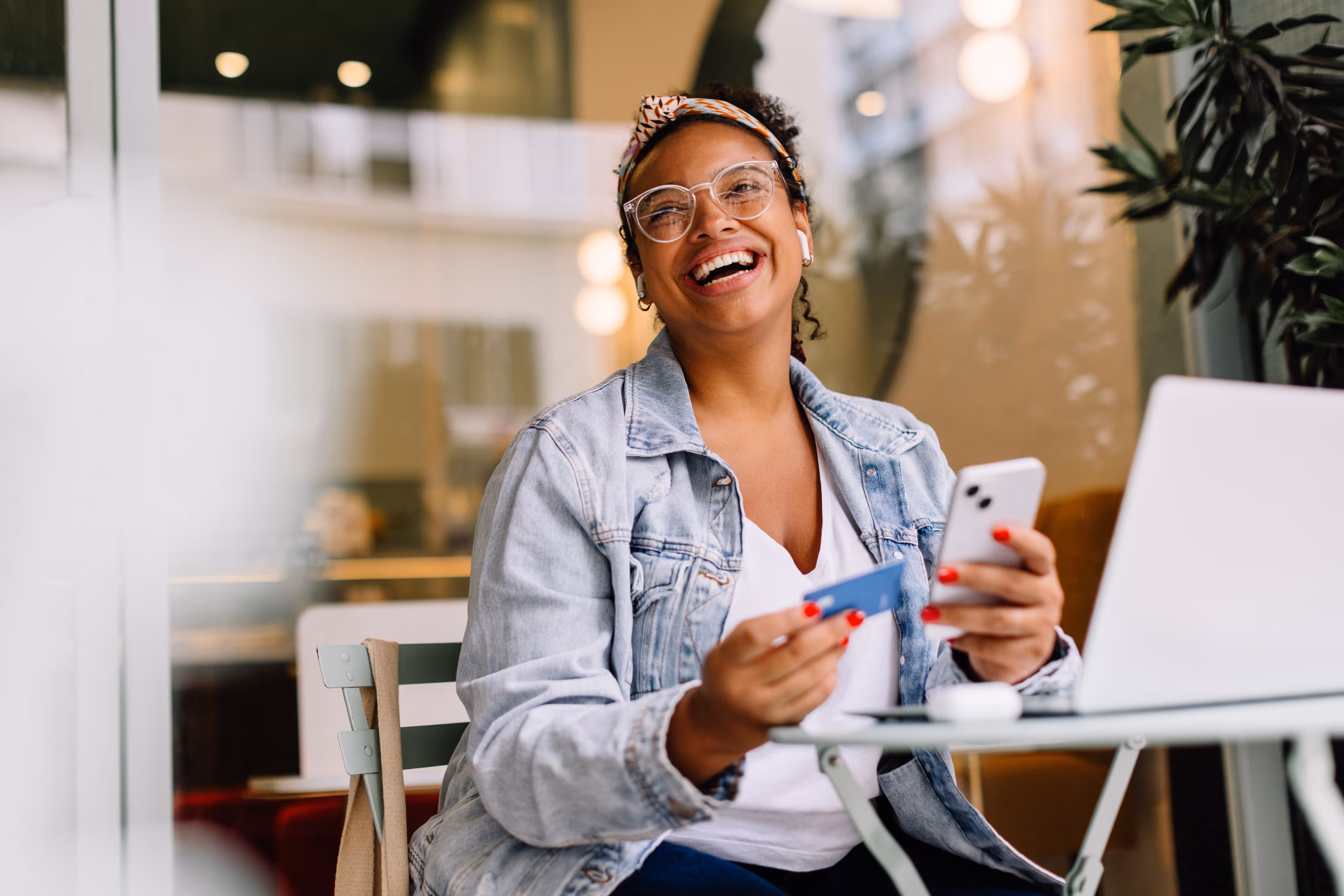 woman holding a credit card and a phone laughing.