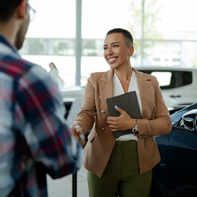 woman at a car dealership shaking a man's hand.