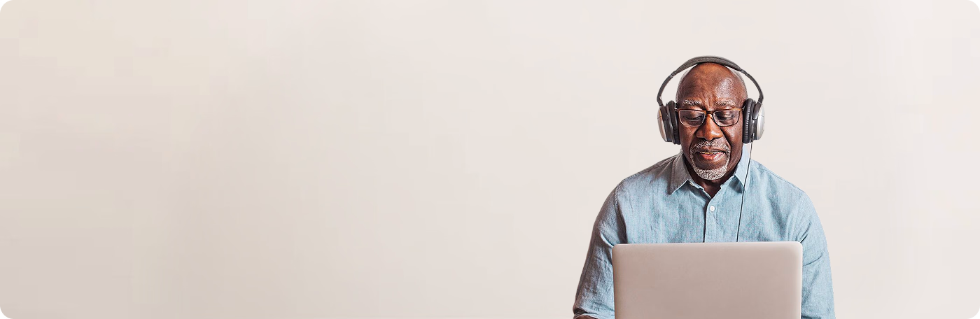 Older man wearing headphones and glasses, working on a laptop.