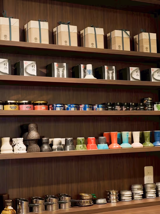 Wooden shelves displaying various packaged products including beige gift boxes with ribbons, decorative ceramic items, and small containers of spices or condiments.