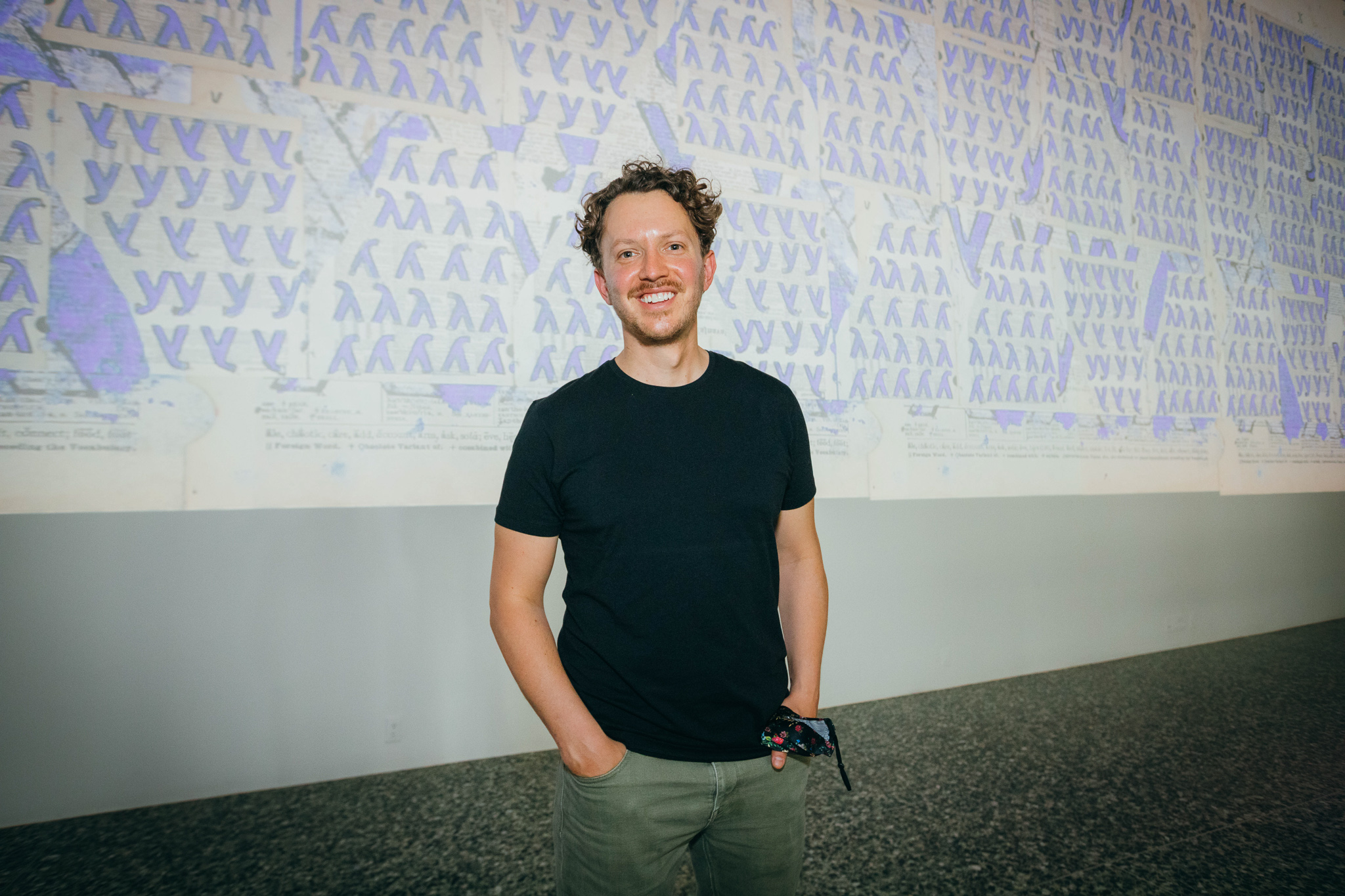 A man in a black shirt poses in front of a wall with a projected image behind him