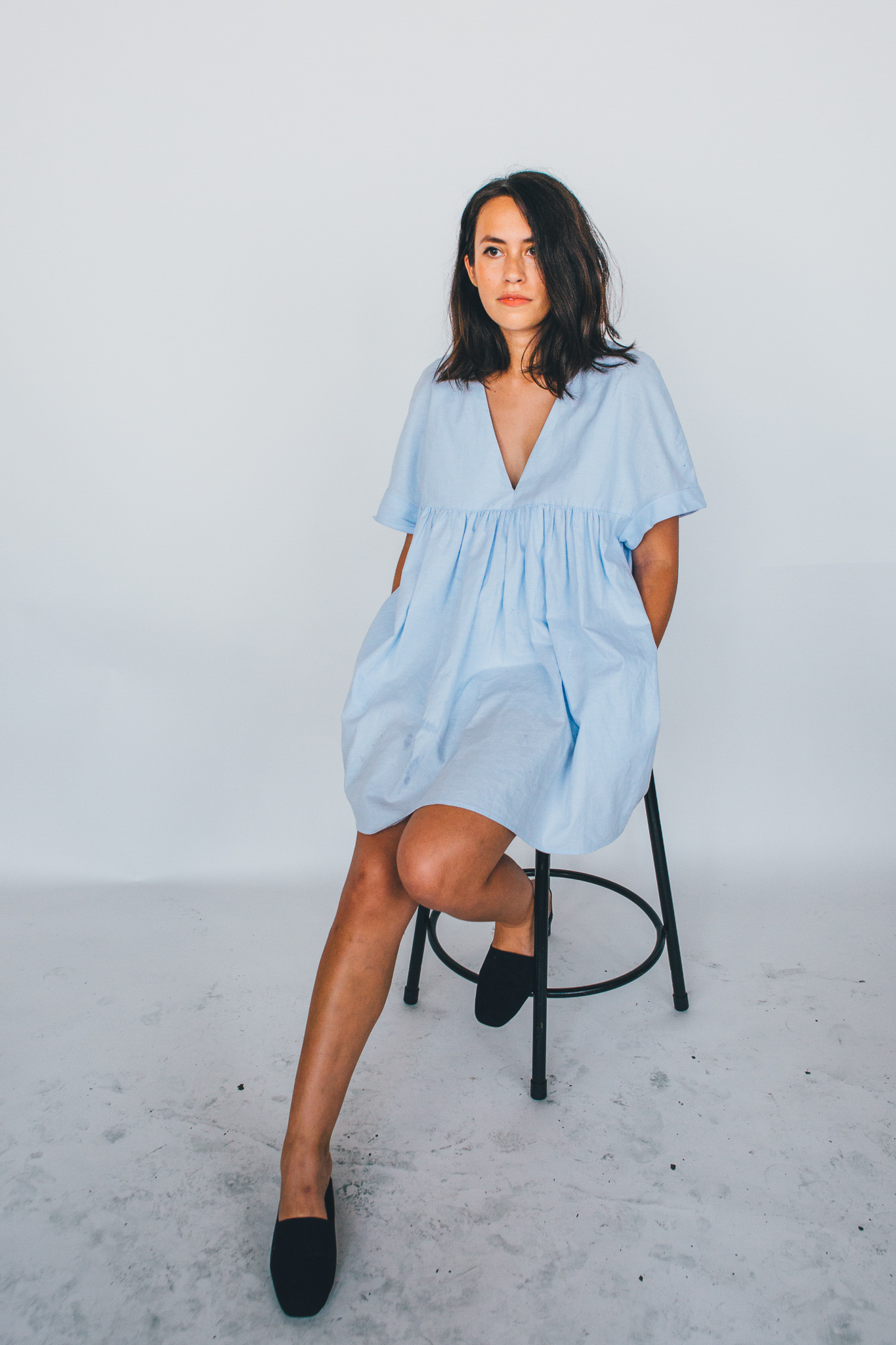 A brunette woman is seated on a stool posing for a portrait photo