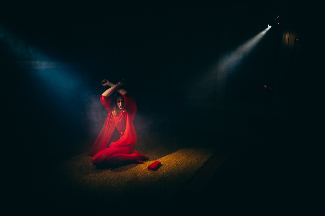 A woman in red is kneeling in dramatic lighting.