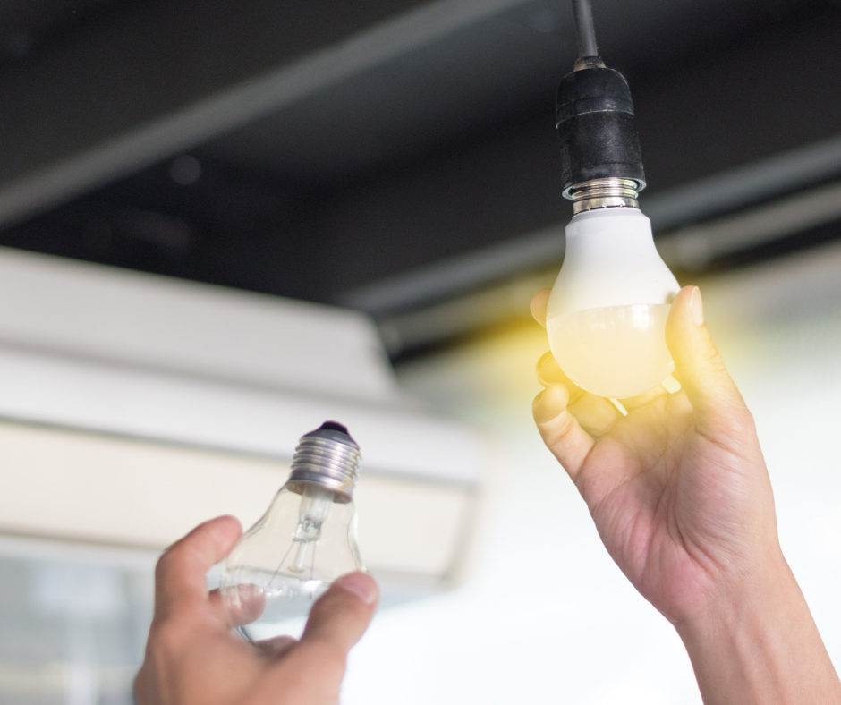 Two hands changing a light bulb one holding the old style light bulb now not screwed in and the other holding the new style lightbulb turned on