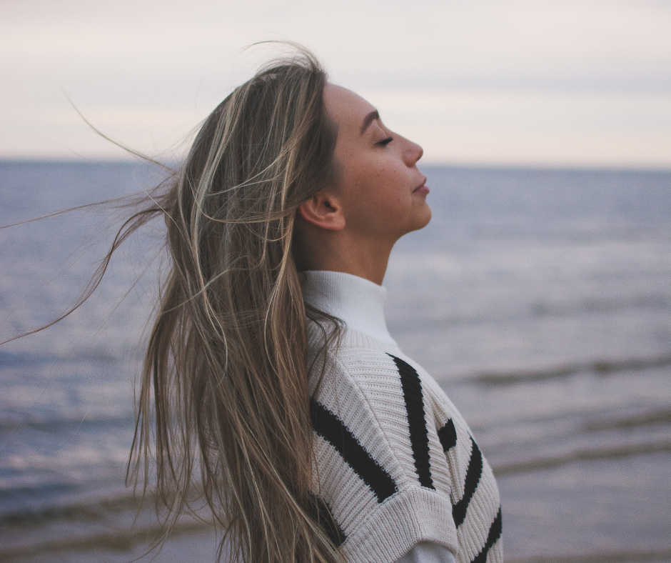 Woman in a black and white striped jumpers stood by the sea taking a deep breath