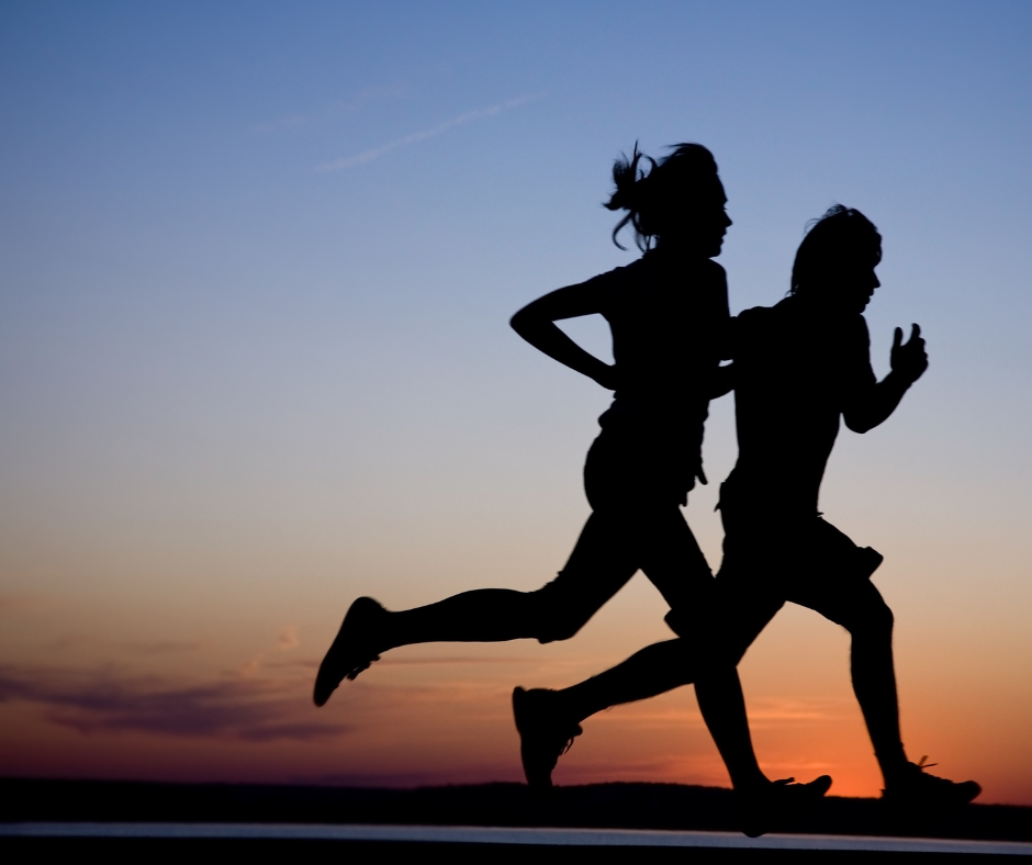Two runners in shadow with a setting sun behind them running on a road