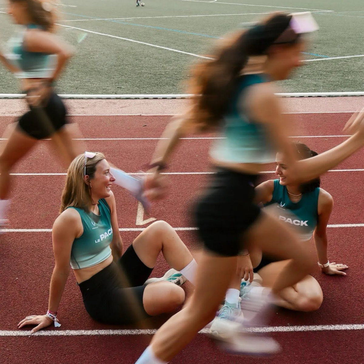 Deux athlètes se reposent sur une piste d’athlétisme pendant qu’une coureuse passe devant elles