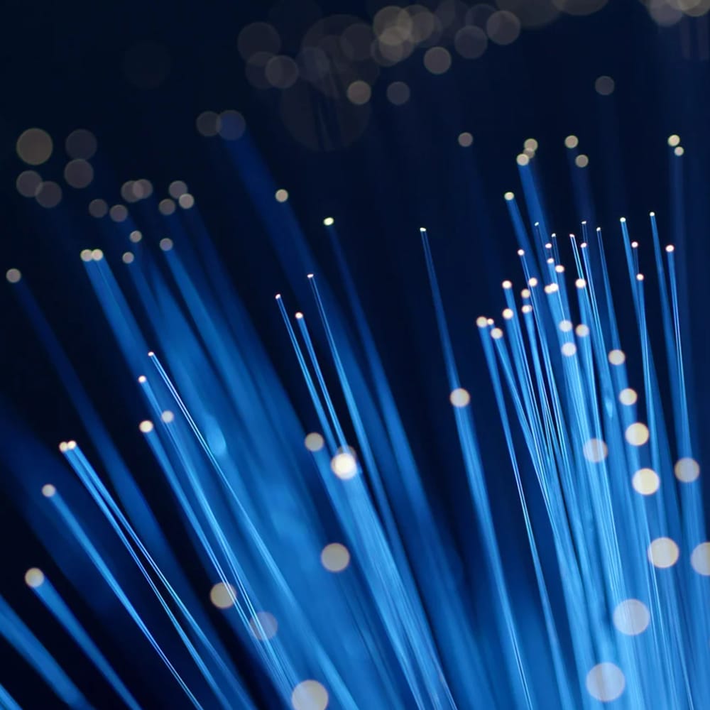 Gros plan sur des brins de fibre optique bleus émettant de la lumière avec des reflets bokeh circulaires sur un fond sombre.