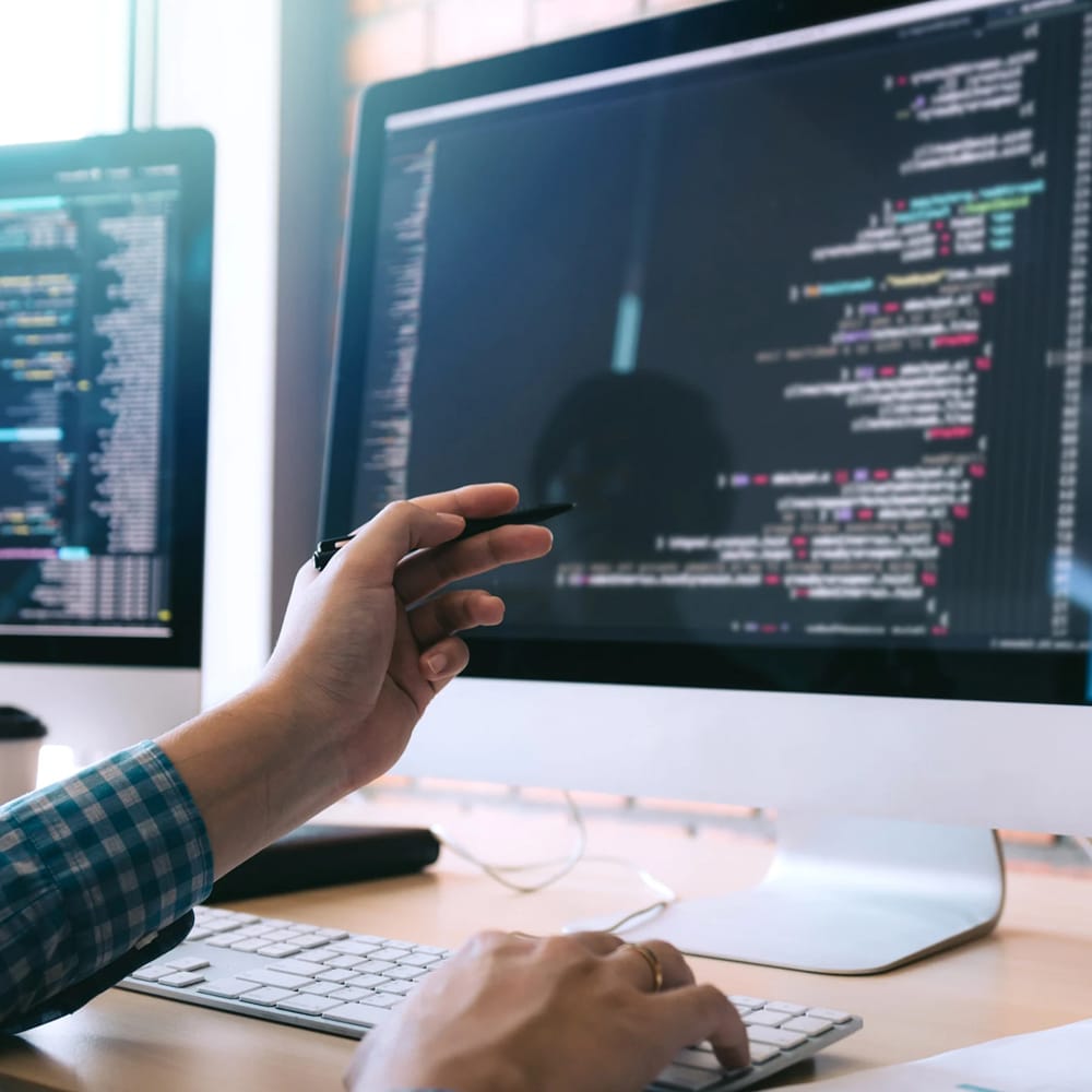 Personne pointant d'une main le code affiché sur l'écran d'un ordinateur de bureau tout en tapant de l'autre main sur le clavier.