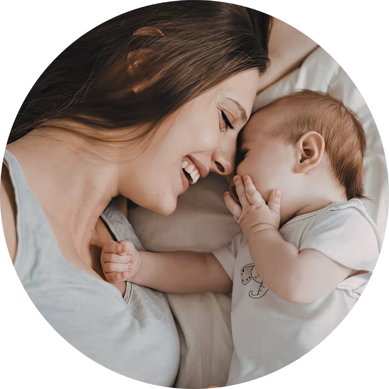 Smiling woman lying face-to-face with a baby who has a hand near their mouth.