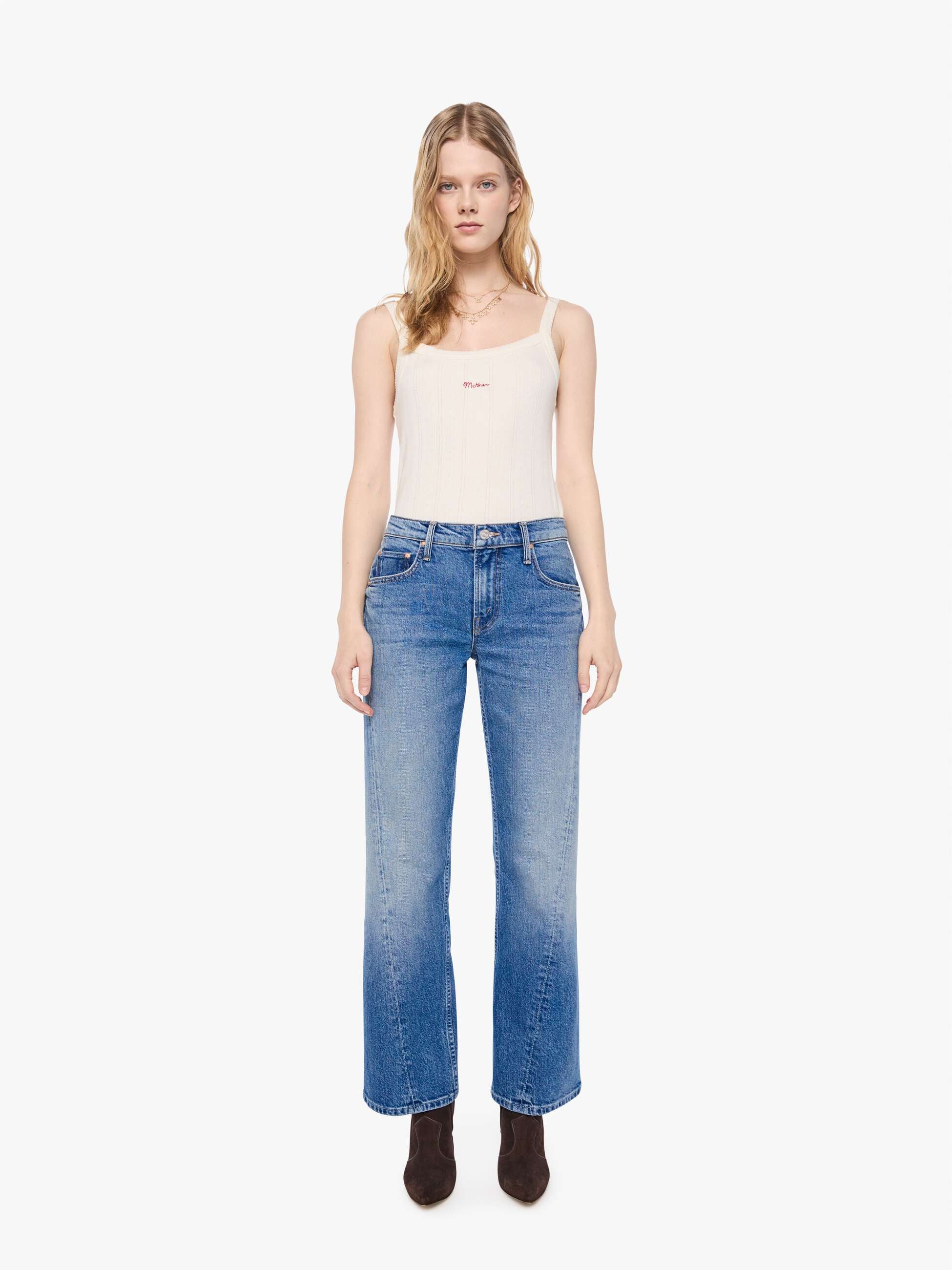 Front view of a petite woman in a mid-blue mid-rise bootcut with a zip fly, looser leg, twisted outer seam and a long 28-inch inseam with a clean hem.