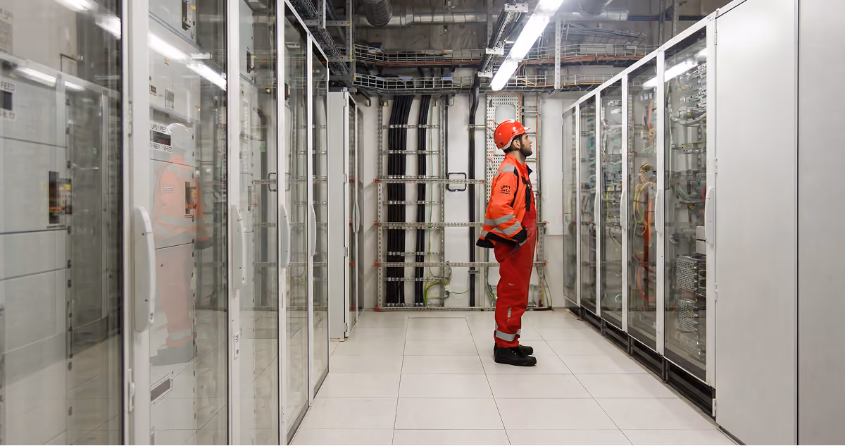 A construction worker in red safety gear inspecting data center infrastructure inside a server room.