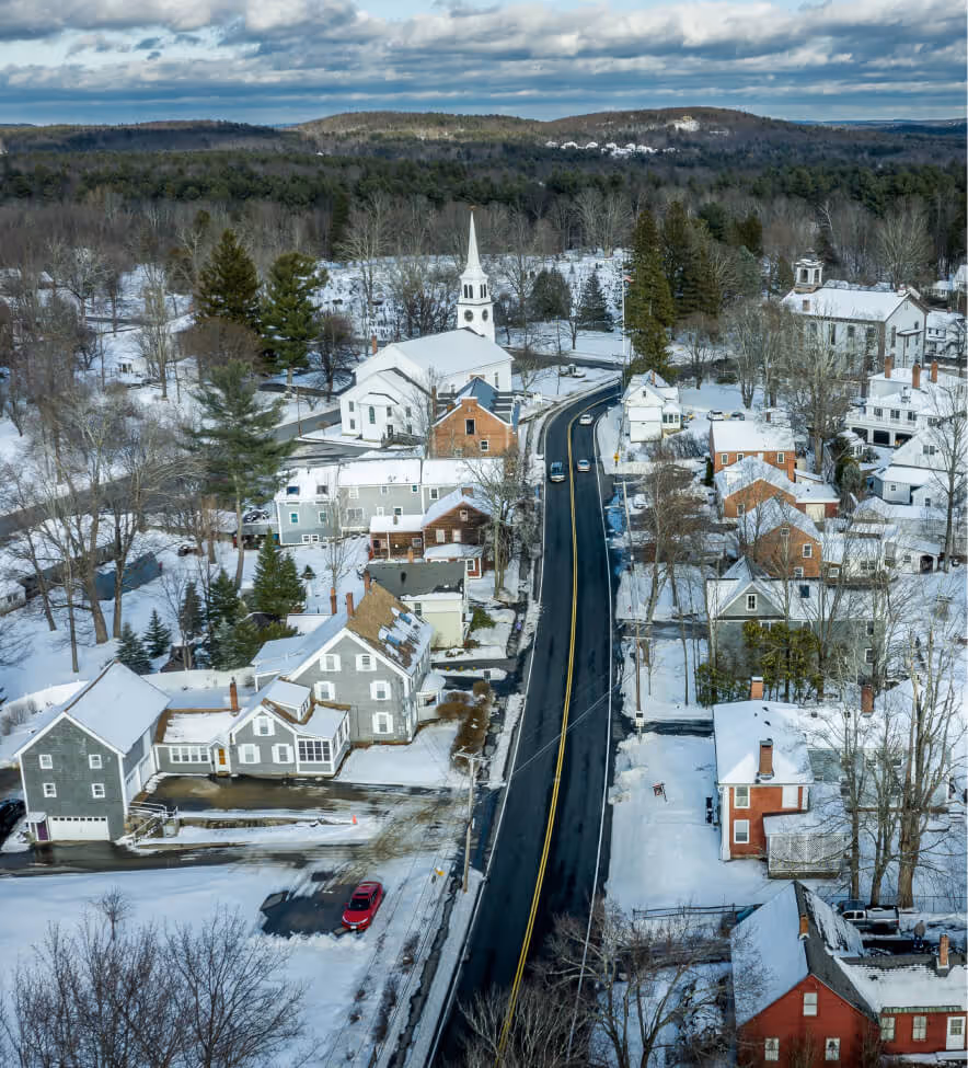 Aerial view of a small snowy town with houses, a church, and a road running through the center.