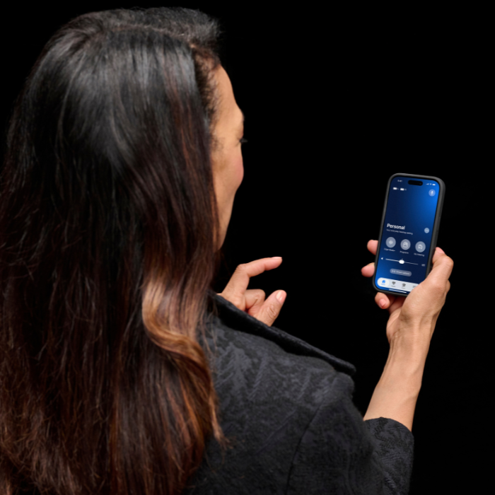 Person using a smartphone hearing aid app to adjust listening settings, manage hearing aid controls, and personalize the hearing experience from a mobile device.